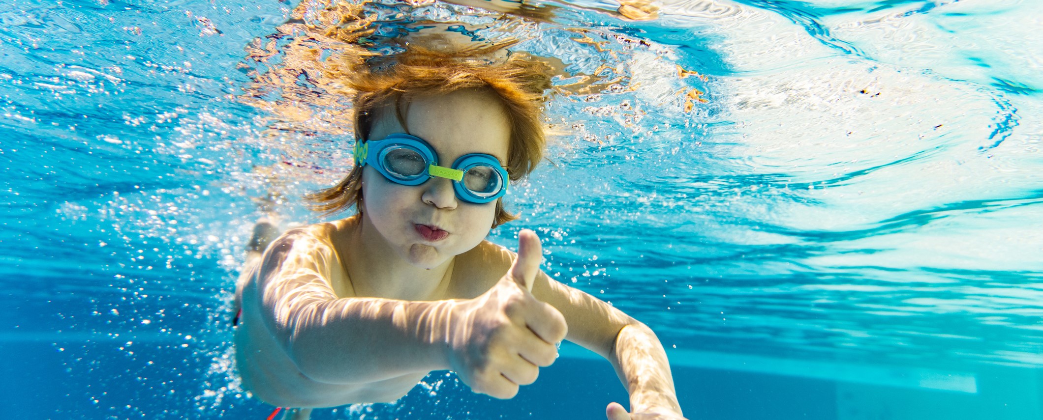 Un enfant dans une piscine avec le pouce levé. 